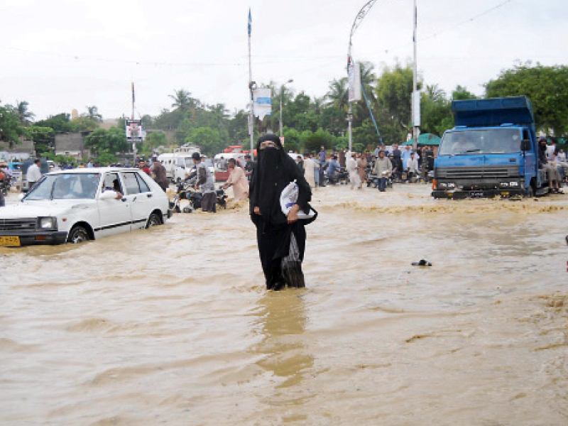 The torrential rain in the city has caused a lot of inconvenience for the citizens. A woman is seen trying to walk through a road submerged in rainwater at KDA Chowrangi. PHOTO: MOHAMMAD NOMAN/EXPRESS