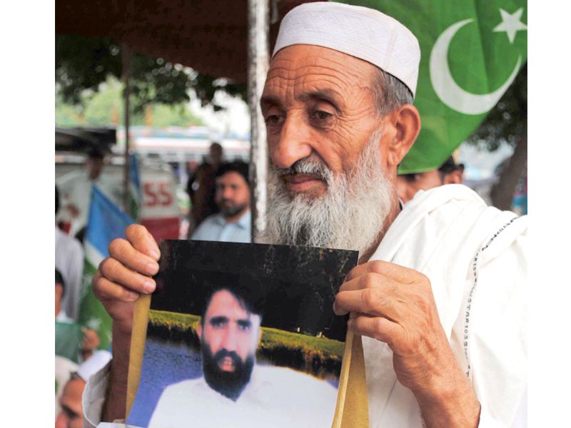 An elderly person holds a photo of his missing son at a protest. PHOTO: MUHAMMAD IQBAL/EXPRESS