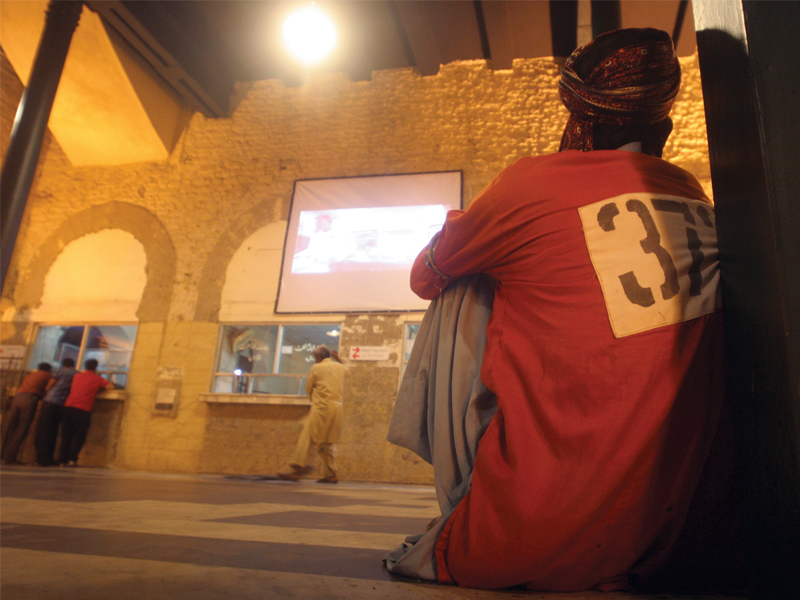 A porter at Karachi Cantonment Railway Station watches a series of movies on Karachi at a mobile cinema set up inside the premises on Sunday night. PHOTO: ATHAR KHAN/EXPRESS