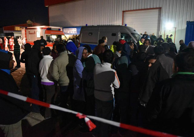 Refugees stand by rescuers and police officers outside a migrants shelter in Calden, near Kassel, on September 27, 2015 where clashes erupted between hundreds of occupants. PHOTO: AFP