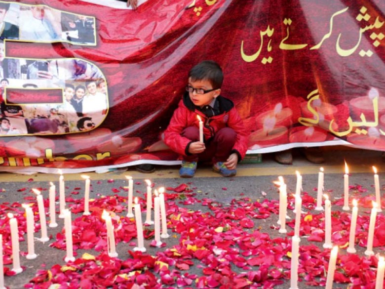 A boy sits under a banner at a vigil at Liberty Chowk. PHOTO: SHAFIQ MALIK/EXPRESS