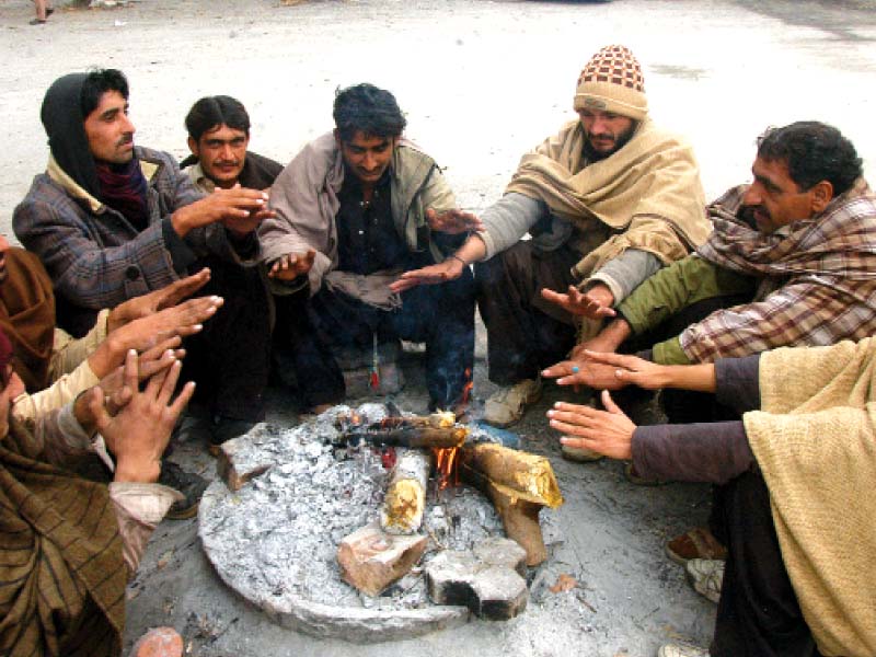 Labourers burn firewood to keep themselves warm, while fog hangs over the capital on Saturday. PHOTOS: WASEEM NAZIR/EXPRESS