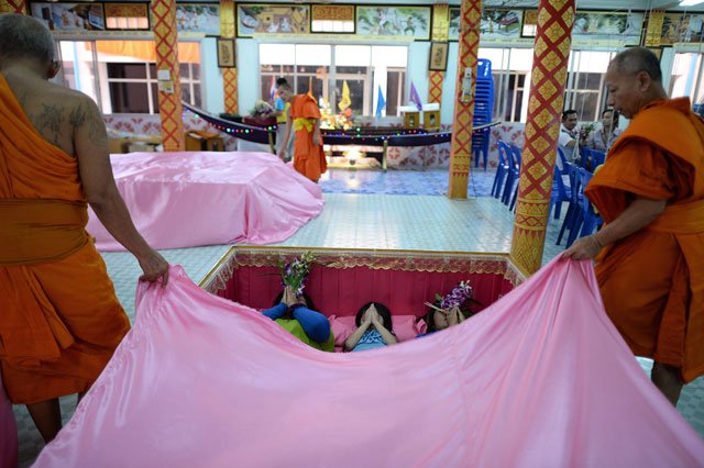 This picture taken on January 16, 2016 shows Buddhist monks draping a pink sheet over members of a family lying in a large coffin during a group resurrection ceremony at the Wat Ta Kien Buddhist temple in Nonthaburi on the outskirts of Bangkok. PHOTO: AFP