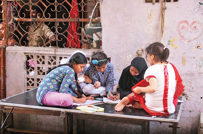Children sit outside their house, doing their homework, in Ranchore Lines during the power shutdown on Friday. PHOTO: ONLINE