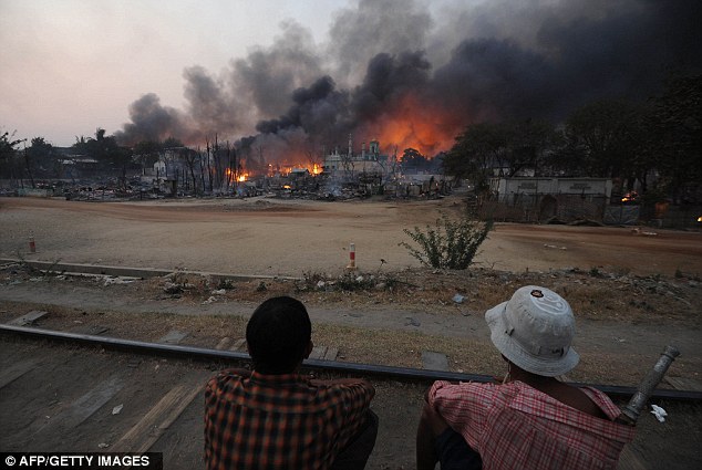 Riots: Two residents sit on a railway track as a mosque burns in riot-hit Meikhtila, central Myanmar.