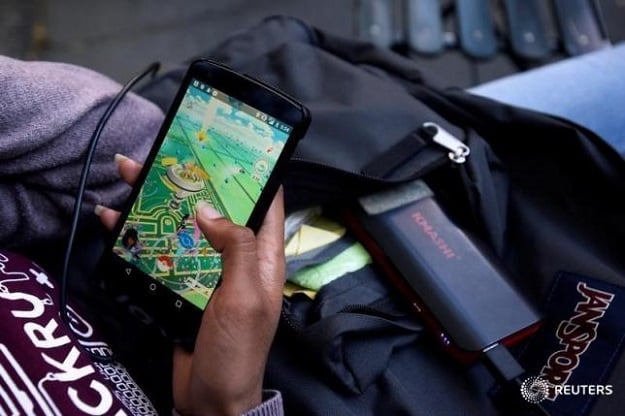 A woman uses a portable battery pack to charge her phone while playing the augmented reality mobile game "Pokemon Go" by Nintendo. PHOTO: REUTERS