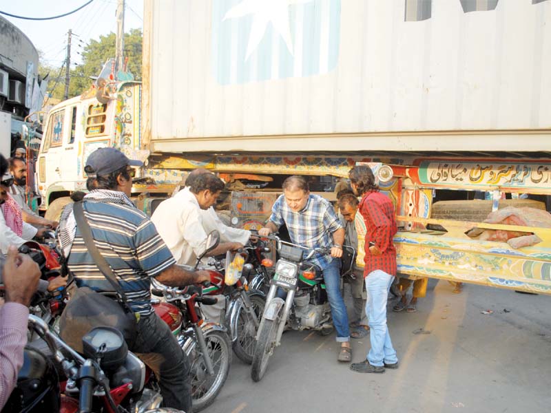 Motorcyclists drive under a container placed on a road along the rally route. PHOTO: ABID NAWAZ/EXPRESS