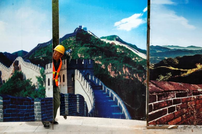 A worker looks through the fence of a construction site that is decorated with pictures of the Great Wall at Badaling, north of Beijing, China. PHOTO: REUTERS