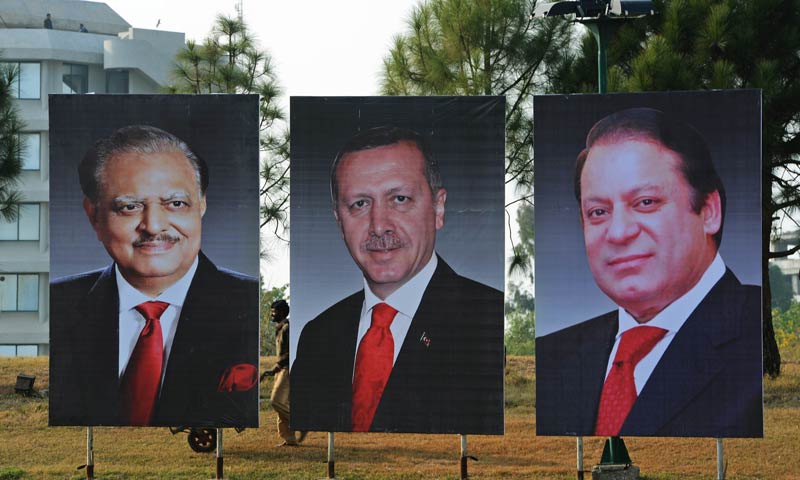 A Pakistani labourer works alongside portraits of Pakistan President Mamnoon Hussain (L) Pakistan Prime Minister Nawaz Sharif (R) and visiting Turkish Prime Minister Recep Tayyip Erdogan (C) on constitution avenue in Islamabad on December 22, 2013. Erdogan is scheduled to pay a two-day official visit to Pakistan from December 23, to discuss economic co-operation between the two countries.   AFP PHOTO/Farooq NAEEM