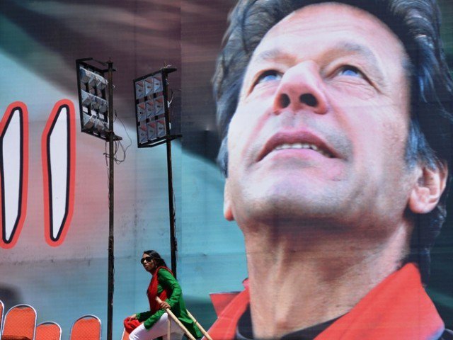 Supporters of Pakistani politician and former cricketer Imran Khan stand next to electoral poster of Khan at the venue of an election campaign meeting by Khan's party Pakistan Tehreek-e-Insaf (PTI) in Islamabad on May 9, 2013. PHOTO: AFP