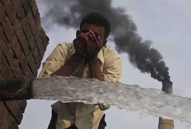 A labourer drinks water as smokes rise from a chimney of a brick factory. PHOTO: REUTERS