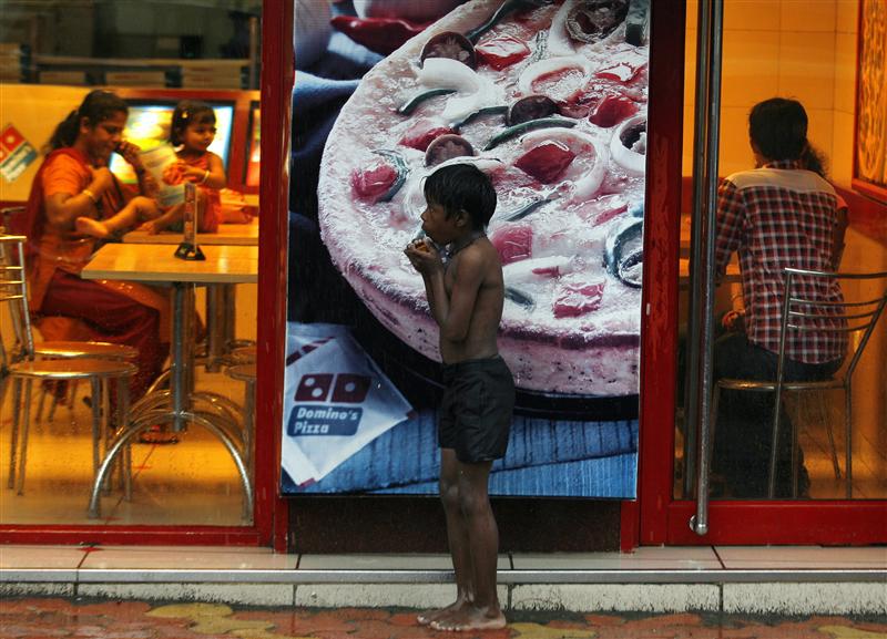 A homeless boy holds biscuits that he received as alms as he takes shelter from rain in front of a fast food shop in Mumbai. PHOTO: REUTERS