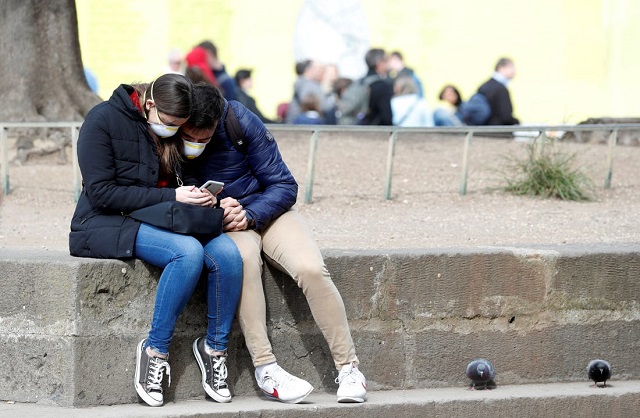 A file photo of a couple wearing protective masks look at a phone next to the Colosseum in Rome. REUTERS