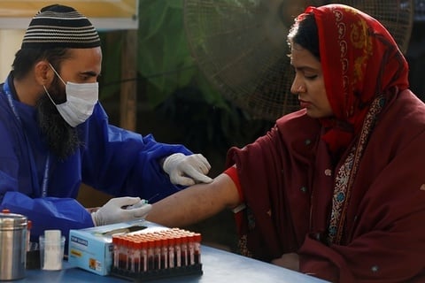 A paramedic wearing protective gloves prepares to take a blood sample from a woman, to be tested for the coronavirus disease (COVID-19) anti-body test, at a camp in Karachi. PHOTO: REUTERS